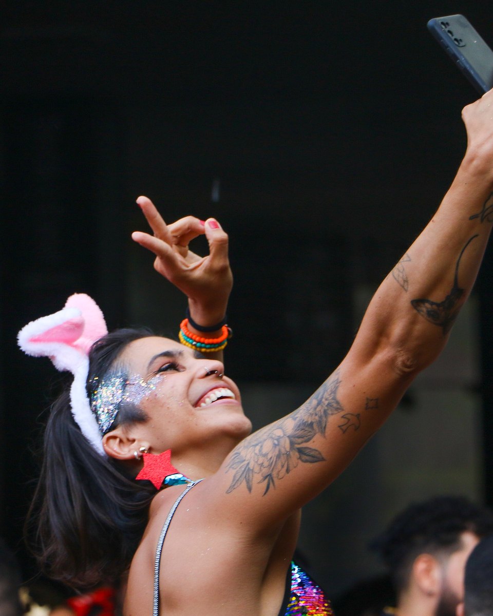 Foliã com tiara de orelhas de coelho, glitter prateado no rosto e braço tatuado fazendo uma selfie com o celular no alto durante um bloco no Setor Comercial Sul, em Brasília.