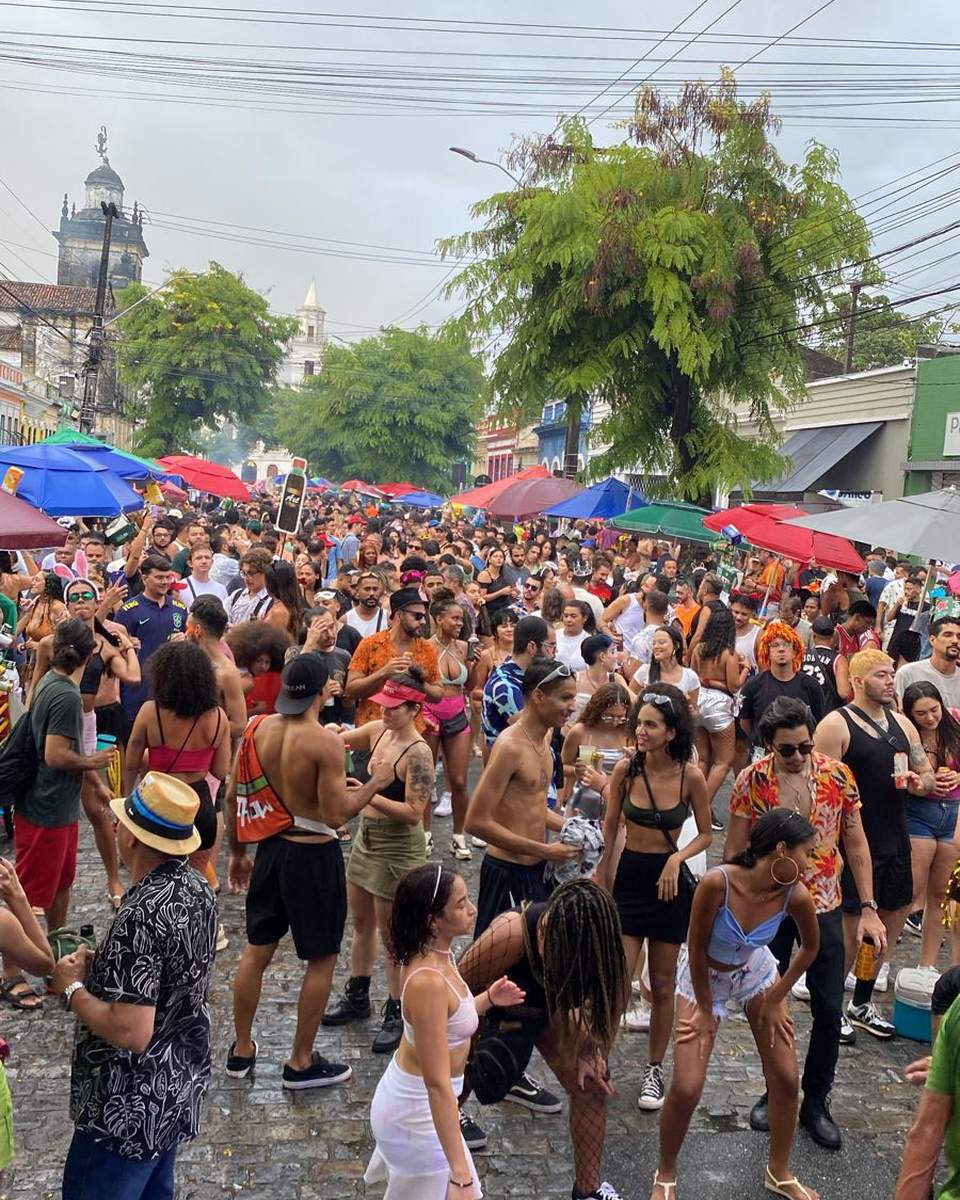 Multidão de foliões tomando uma ladeira de paralelepípedo no Centro Histórico de João Pessoa, com guarda-sóis coloridos e as torres das igrejas antigas ao fundo.