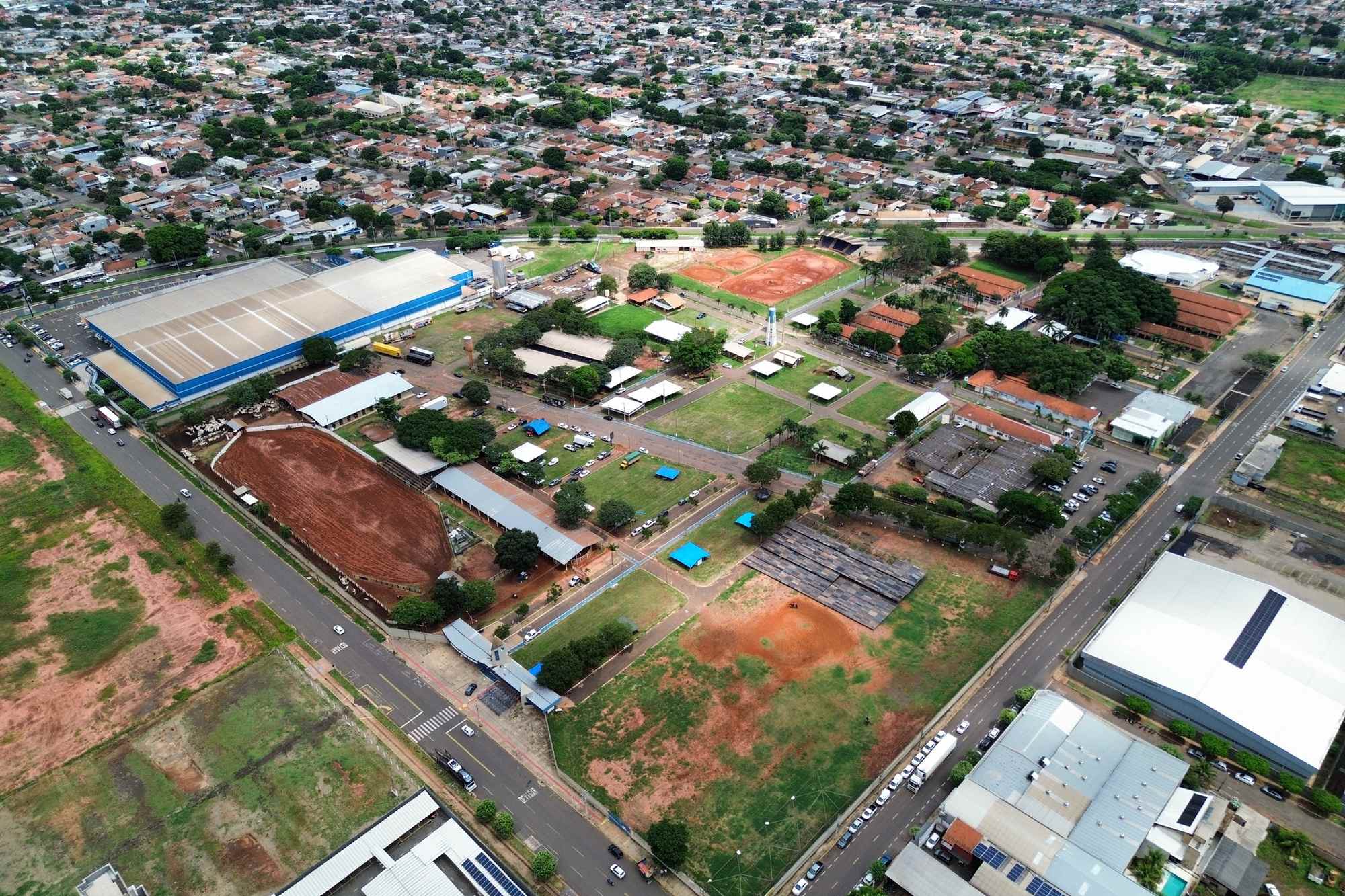 Vista aérea do Parque de Exposições Laucídio Coelho, em Campo Grande, com a pista de areia, os galpões de telhado vermelho e os bairros da cidade em volta.
