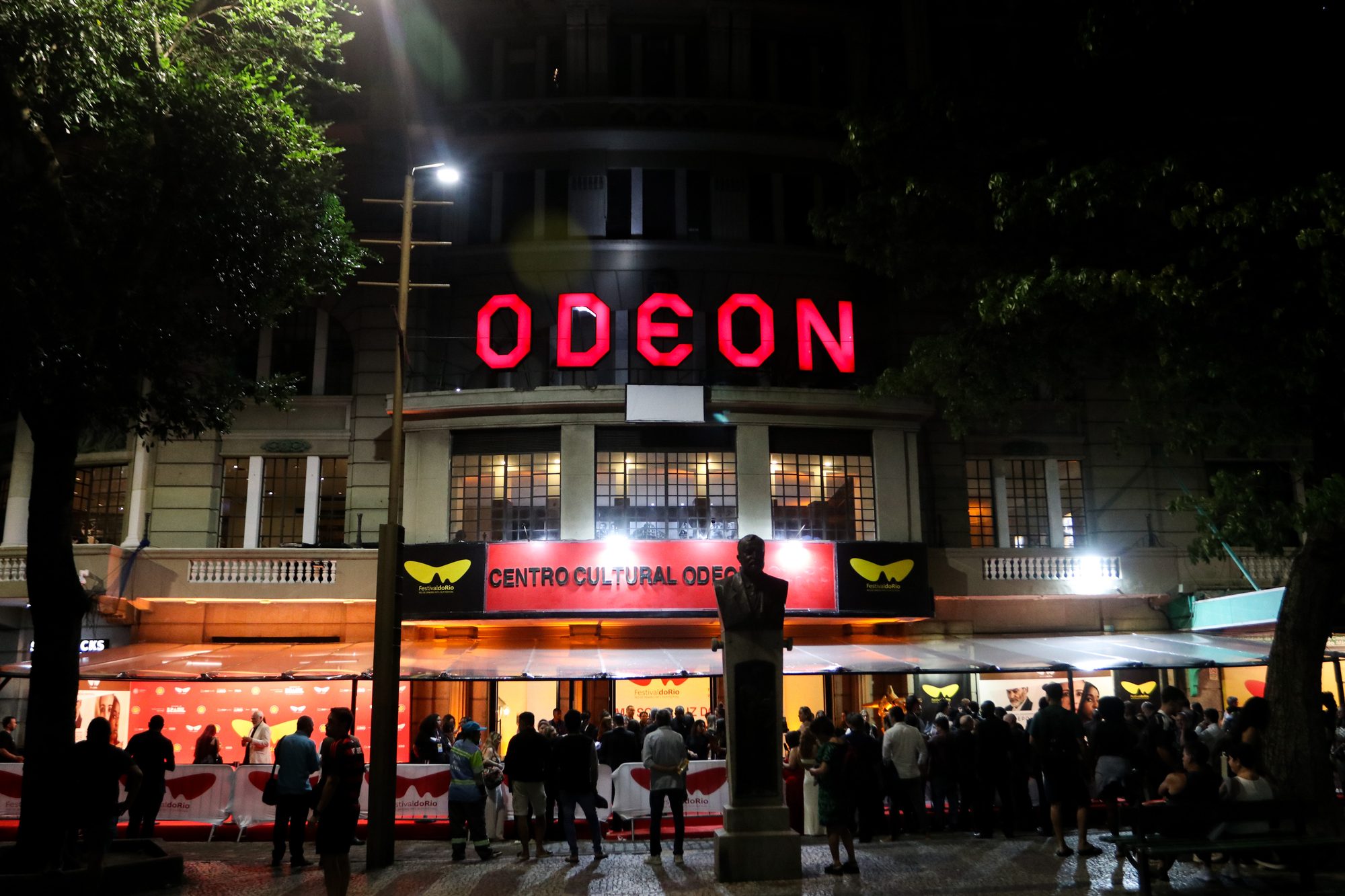 Fachada iluminada do Cine Odeon, na Cinelândia, no Rio de Janeiro, com o letreiro vermelho aceso e o público reunido na calçada na noite de abertura do Festival do Rio 2025.