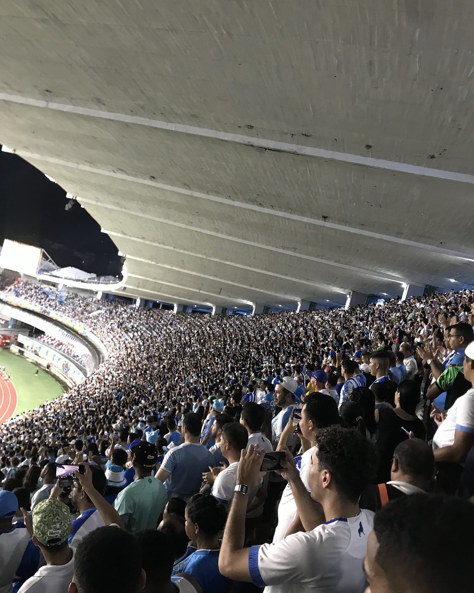 Arquibancada lotada do Mangueirão vista de dentro, com público em pé, celulares levantados e a cobertura de concreto do estádio acima.