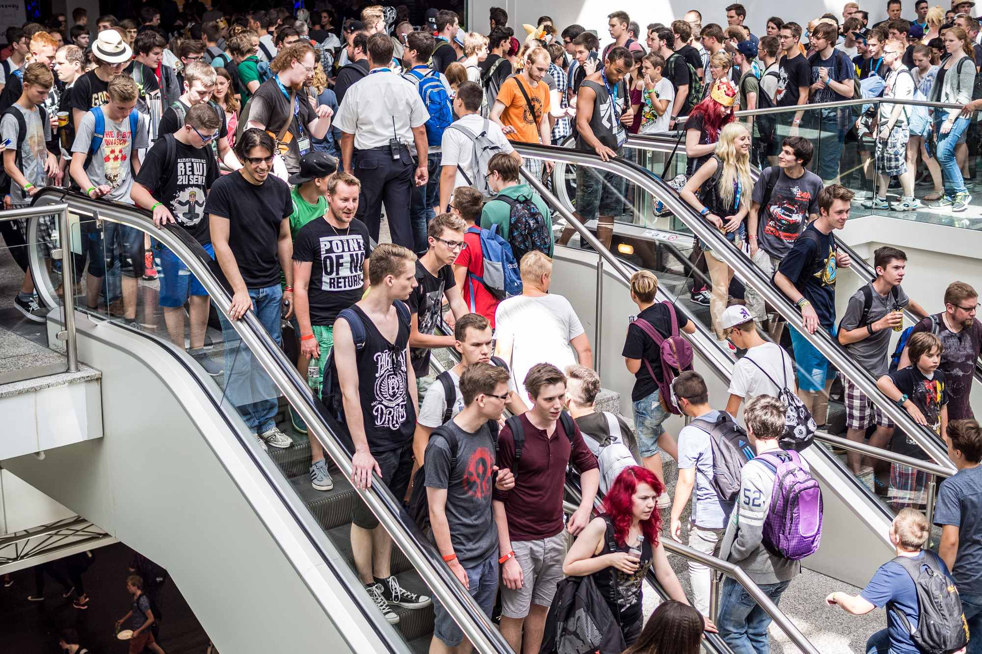 Multidão de jovens de mochila e camiseta preta subindo e descendo escadas rolantes num pavilhão da gamescom, em Colônia, na Alemanha.