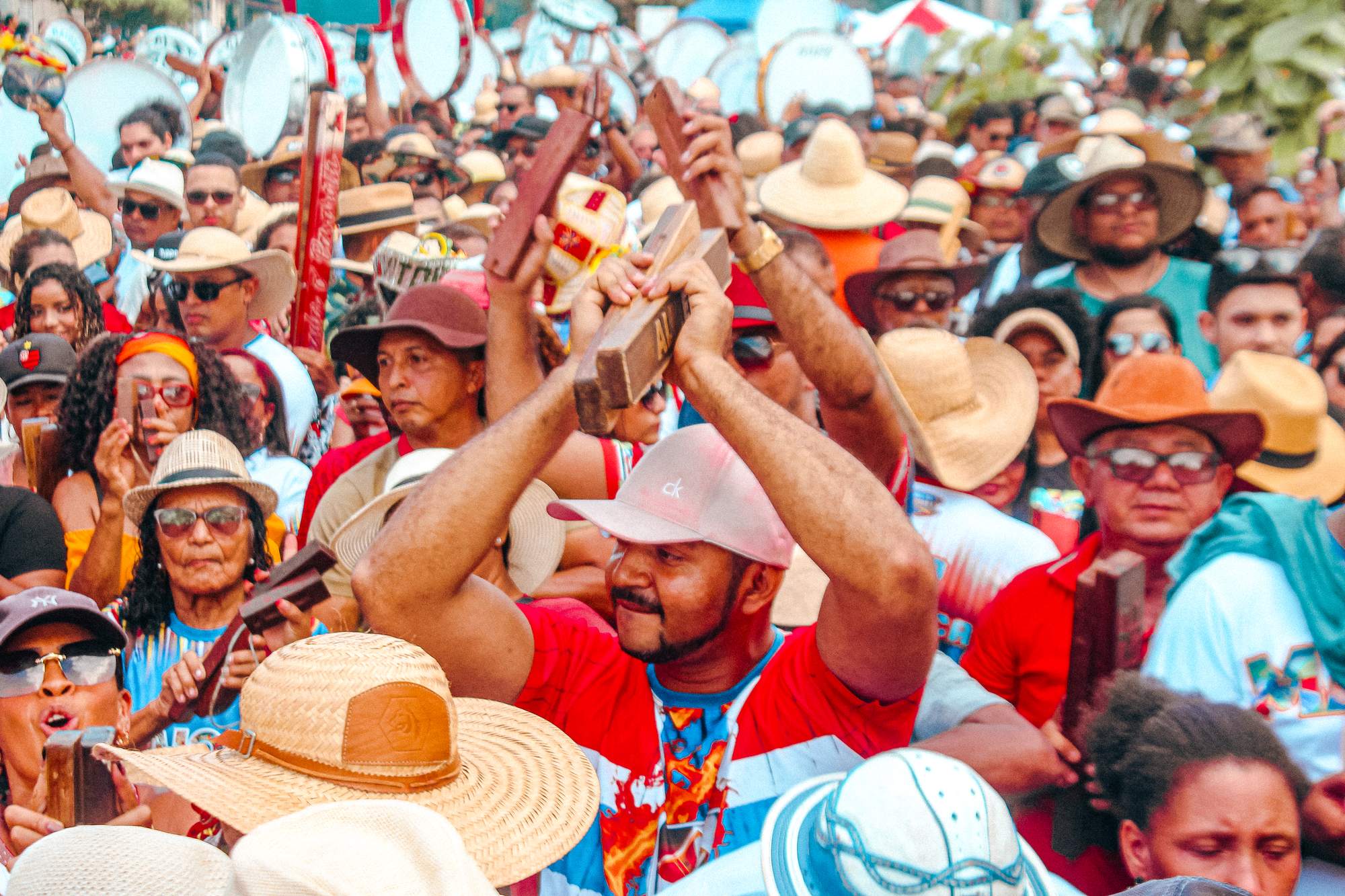 Multidão de brincantes de chapéu de palha tocando matracas de madeira e pandeirões numa rua de São Luís, durante o arrastão do Boi da Maioba, grupo de bumba meu boi do sotaque de matraca.