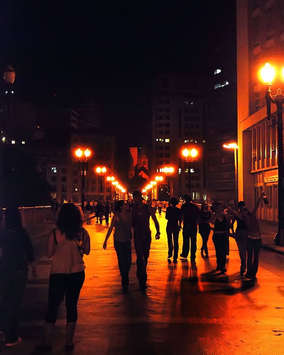 Grupo de pessoas caminhando à noite por um viaduto iluminado por postes laranja no centro de São Paulo, durante a Virada Cultural de 2008.