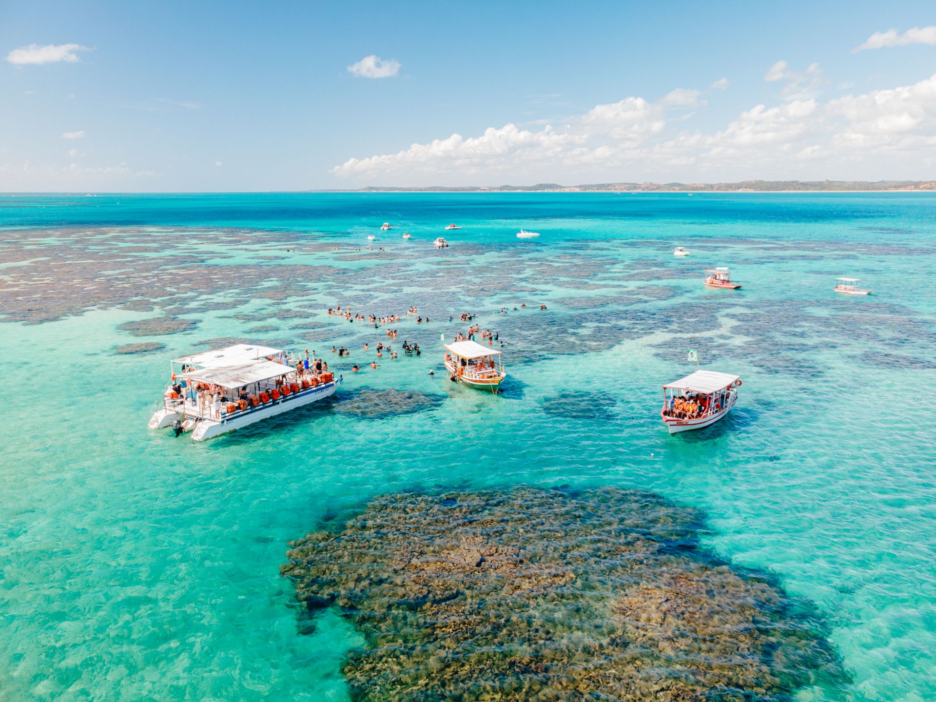 Vista aérea das piscinas naturais de Maragogi, água turquesa sobre os recifes com barcos ancorados