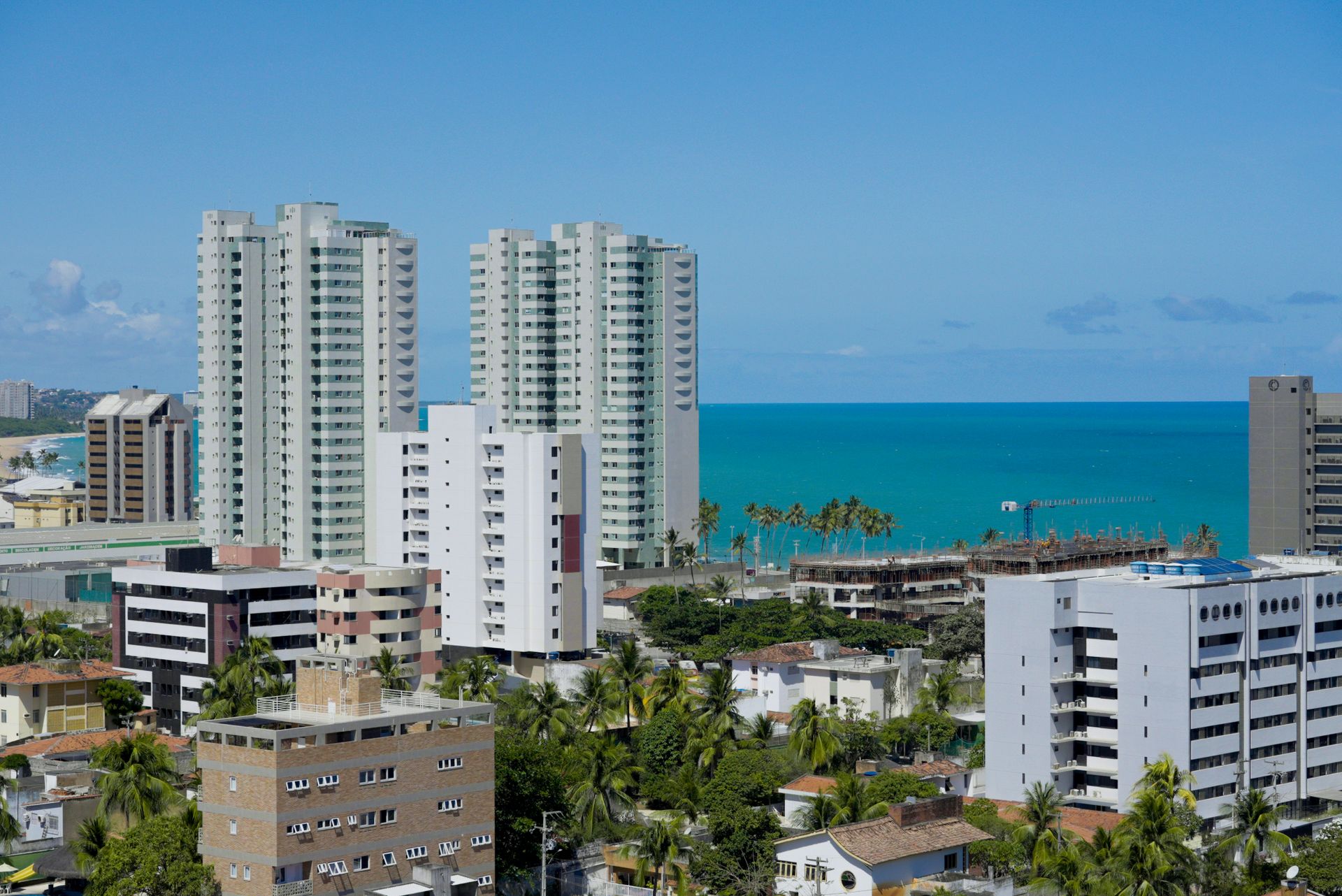 Vista aérea de prédios altos na orla de Maceió com o mar azul-turquesa ao fundo