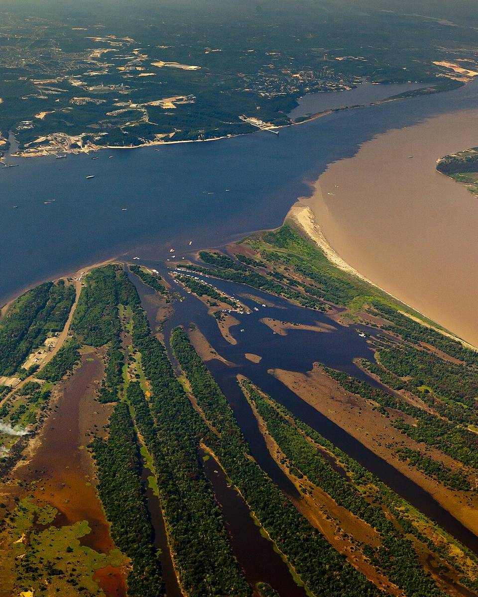 Vista aérea do Encontro das Águas em Manaus, com a linha nítida entre a água escura do rio Negro e a água barrenta do rio Solimões e navios ancorados no trecho escuro.