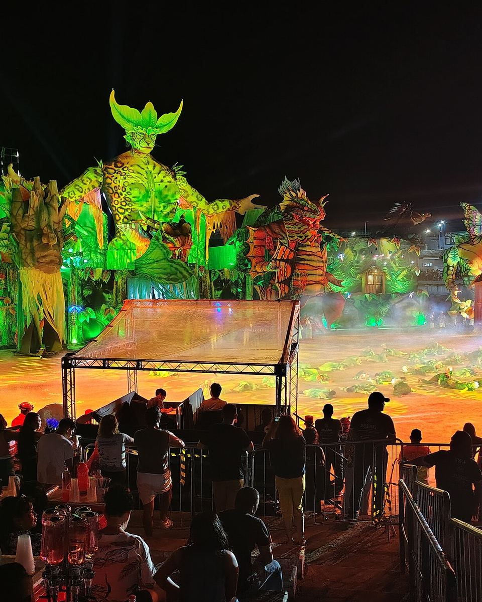 Apresentação noturna no Festival de Cirandas de Manacapuru, com alegorias gigantes iluminadas na arena e o público assistindo das arquibancadas.
