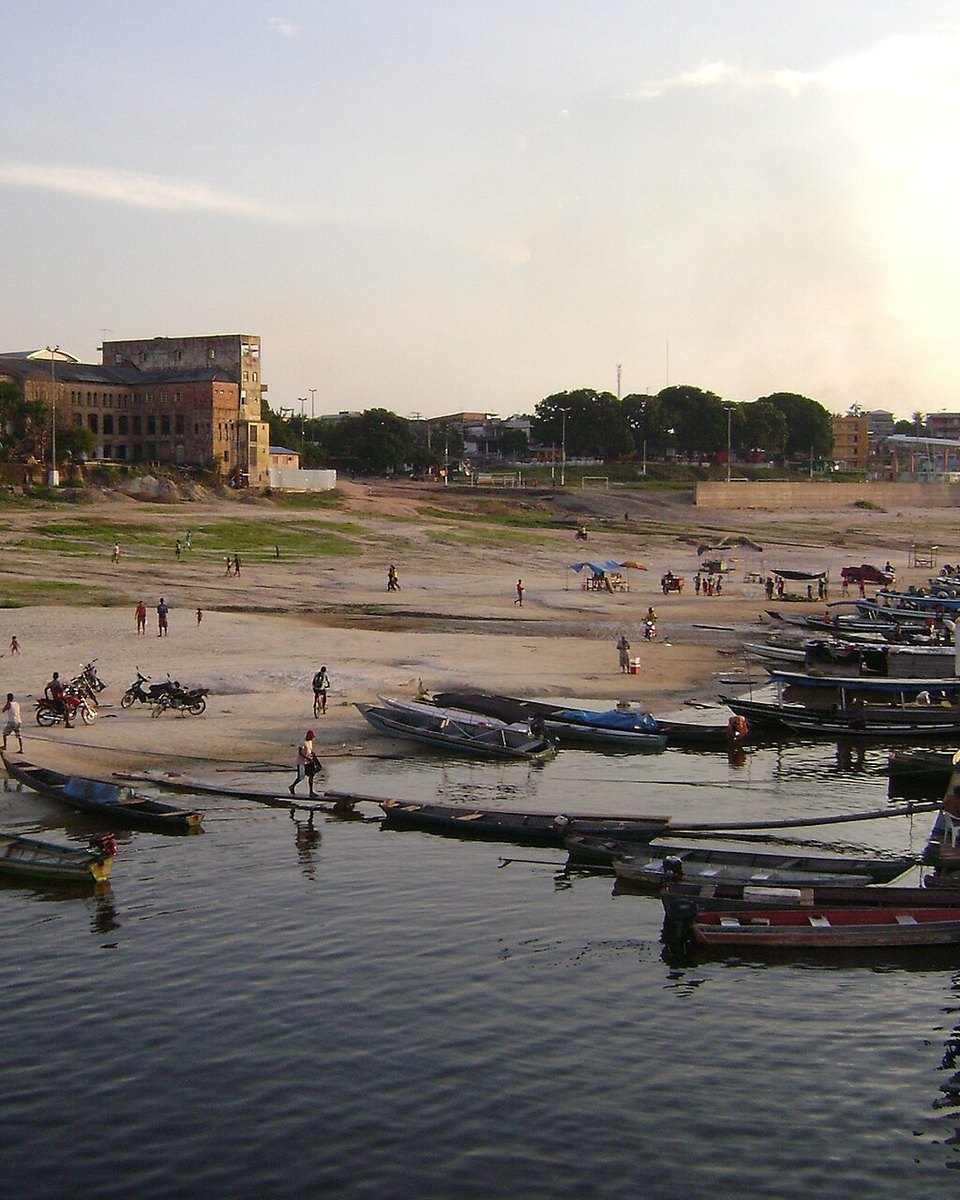 Orla de Tefé no fim da tarde, com dezenas de canoas de madeira encostadas na beira do lago, moradores e motos na faixa de areia e os casarões antigos da cidade ao fundo.