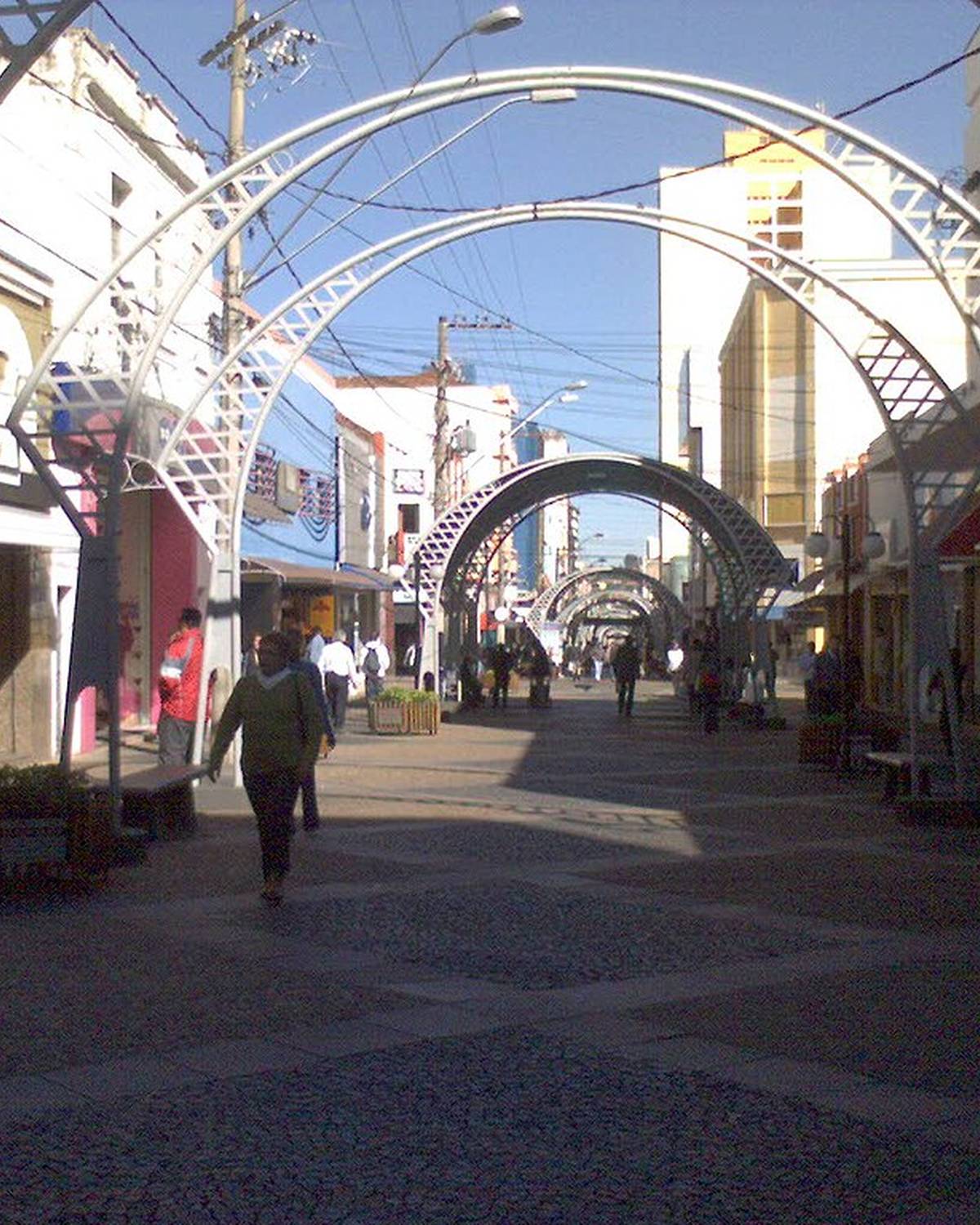 Calçadão da Rua Batista de Carvalho, no Centro de Bauru, com pedestres caminhando entre lojas sob os arcos de ferro que cobrem a rua.