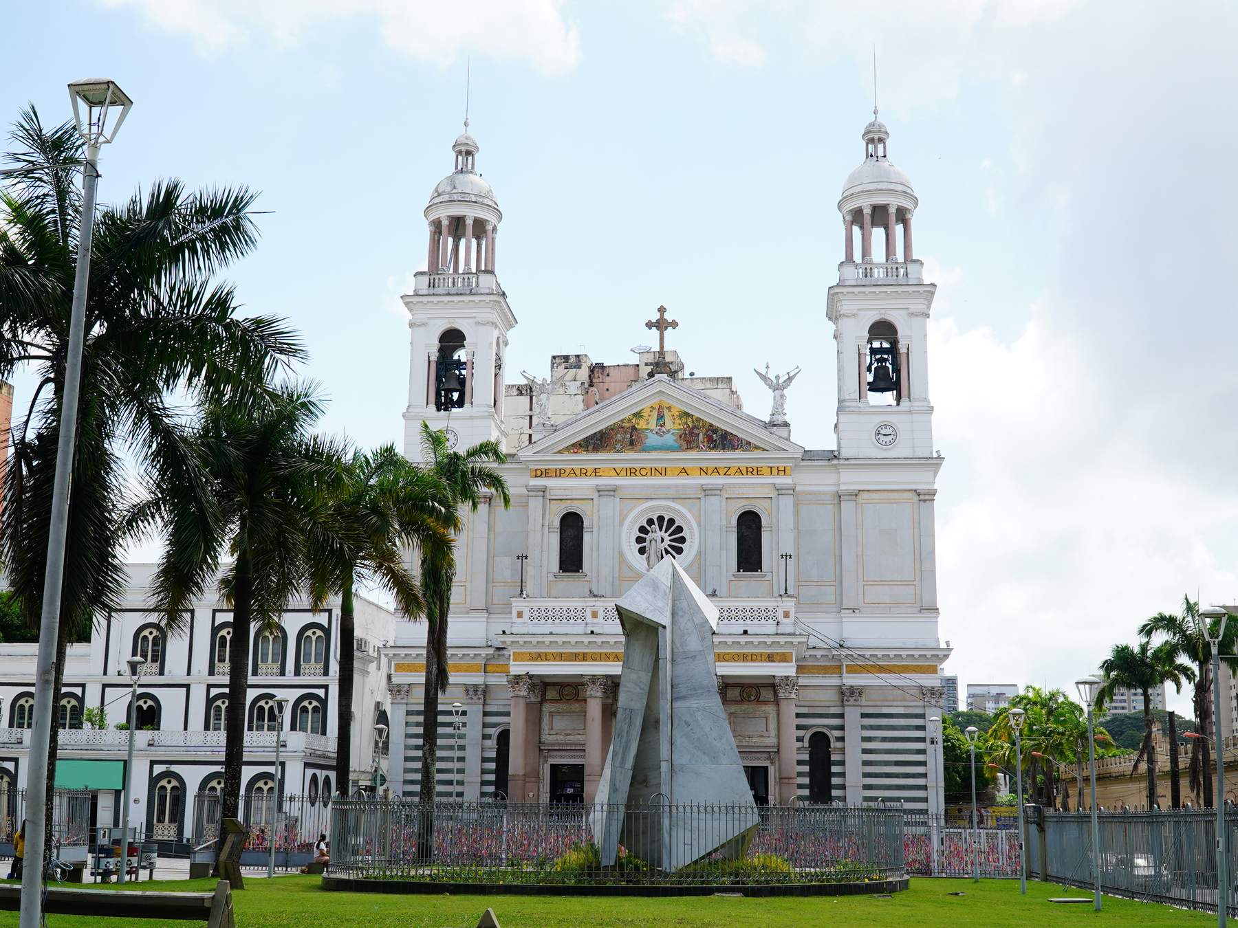 Fachada branca da Basílica Santuário de Nossa Senhora de Nazaré, com as duas torres, palmeiras altas em volta e a praça em frente, num dia de céu azul