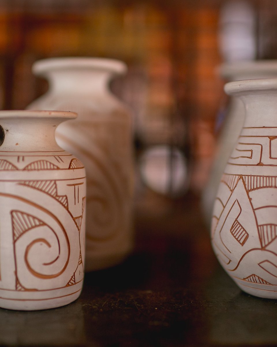 Vasos brancos de cerâmica marajoara com grafismos geométricos vermelhos alinhados na prateleira de um ateliê em Icoaraci.