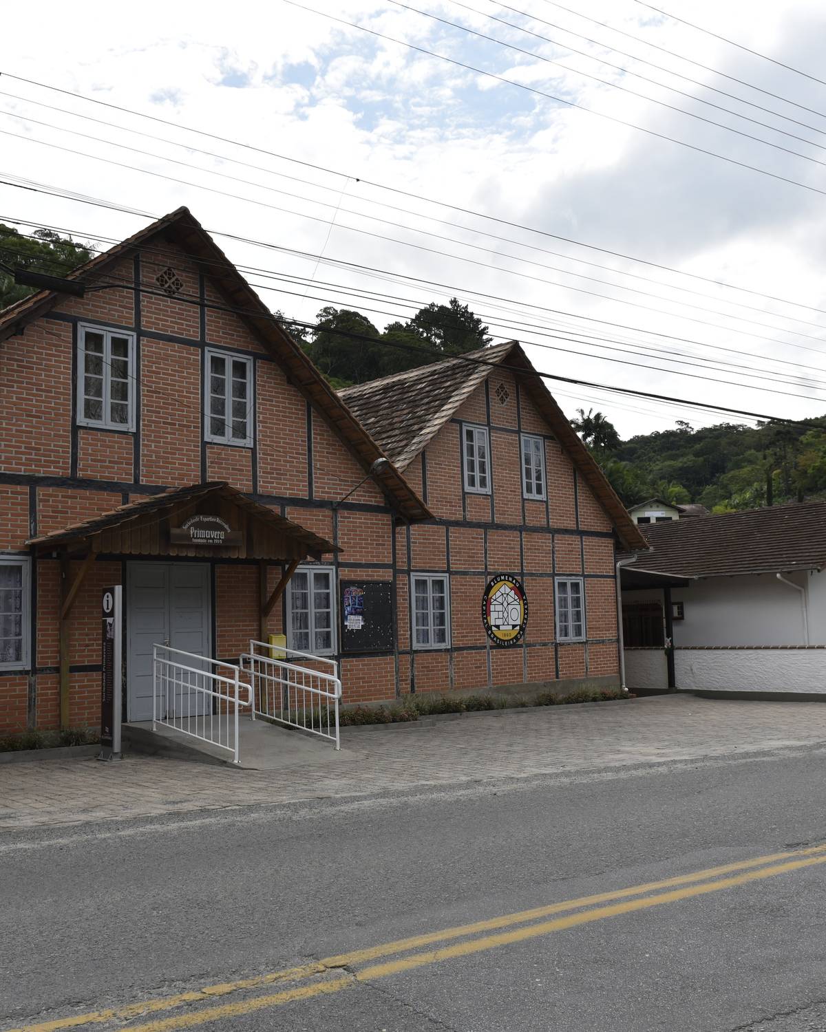 Casas enxaimel de tijolos à beira da rua na Vila Itoupava, distrito rural de Blumenau, com os morros cobertos de mata ao fundo.