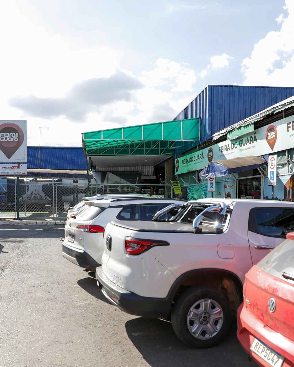 Entrada da Feira do Guará, no Distrito Federal, com o letreiro no alto e carros estacionados em frente.