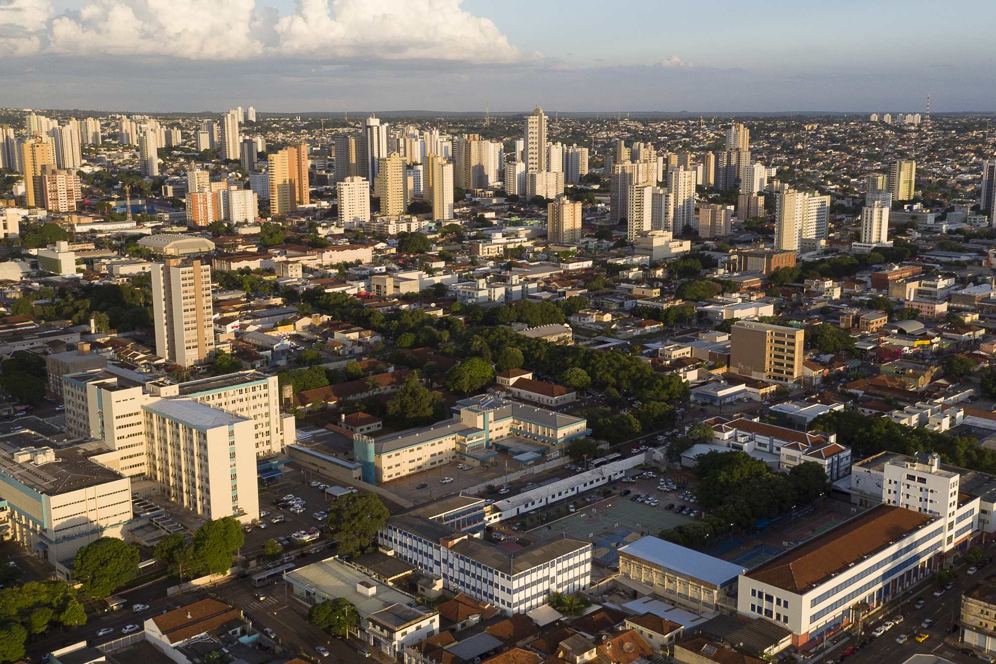 Vista aérea do centro de Campo Grande no fim da tarde, com prédios altos, quarteirões arborizados e a cidade se espalhando plana até o horizonte.
