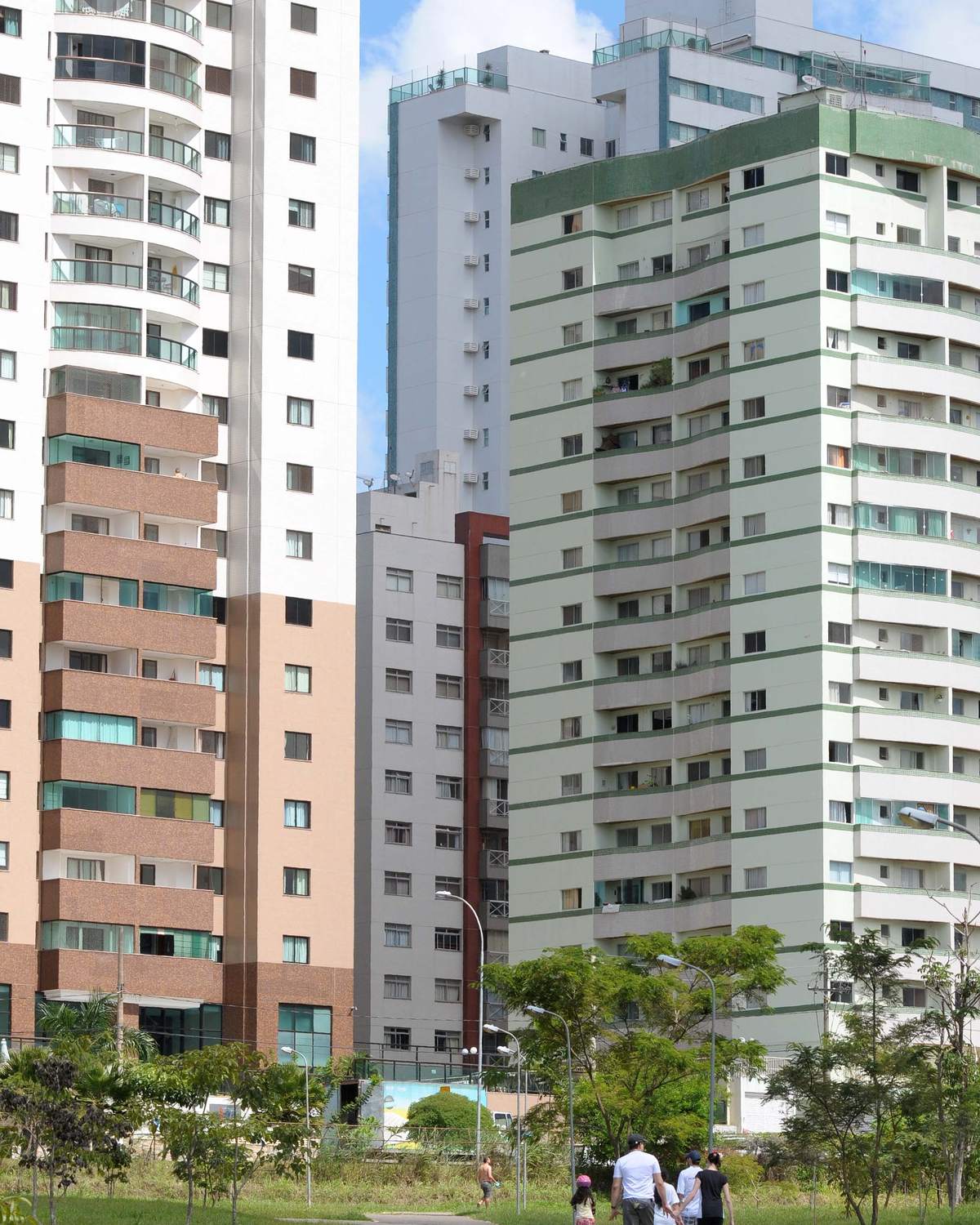Pessoas caminhando por uma pista do Parque de Águas Claras, no gramado, com as torres residenciais da cidade logo atrás.