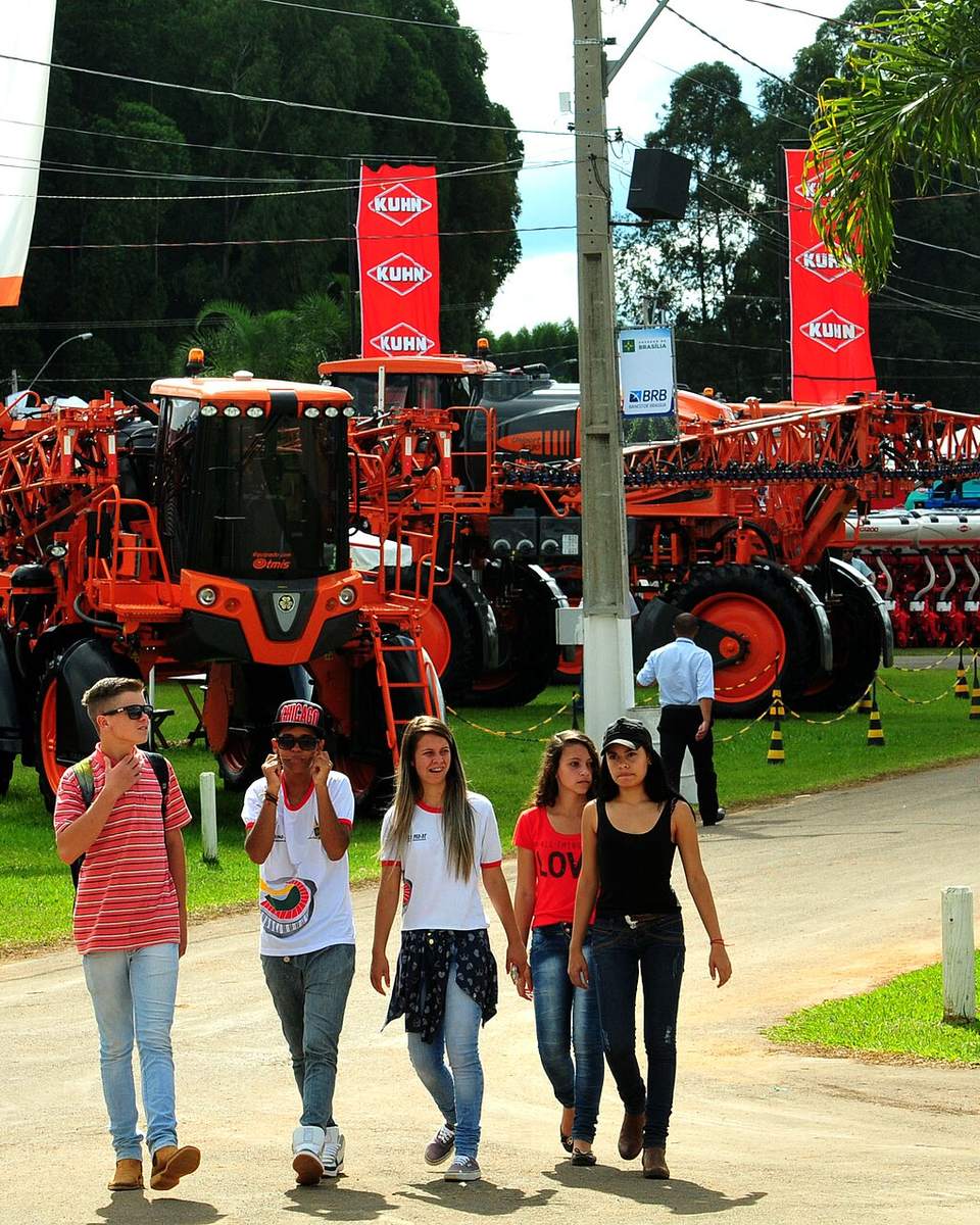 Visitantes caminhando por uma alameda da AgroBrasília, no PAD-DF, entre máquinas agrícolas vermelhas e verdes expostas nos estandes.