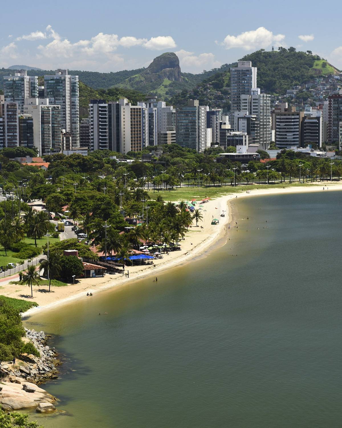 Praia da Curva da Jurema com faixa de areia, avenida arborizada e prédios de Vitória ao fundo.