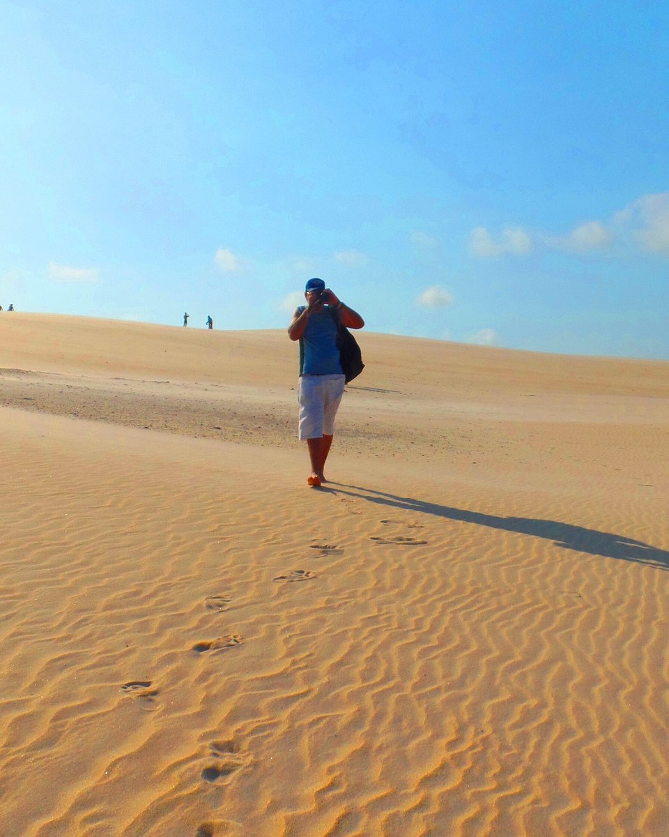 Homem caminhando sozinho sobre as dunas de areia de Itaúnas em dia de céu azul.