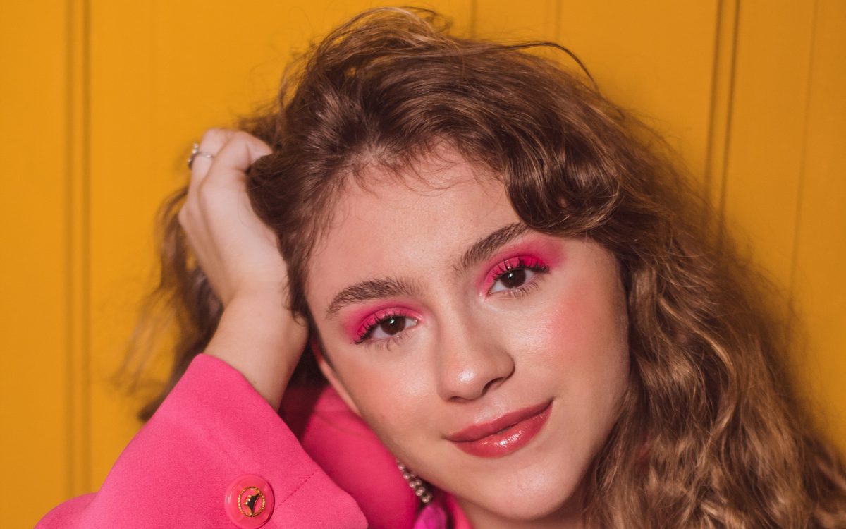 Jovem de blazer rosa e maquiagem rosa sorrindo para a câmera, num ensaio de moda em São Paulo.