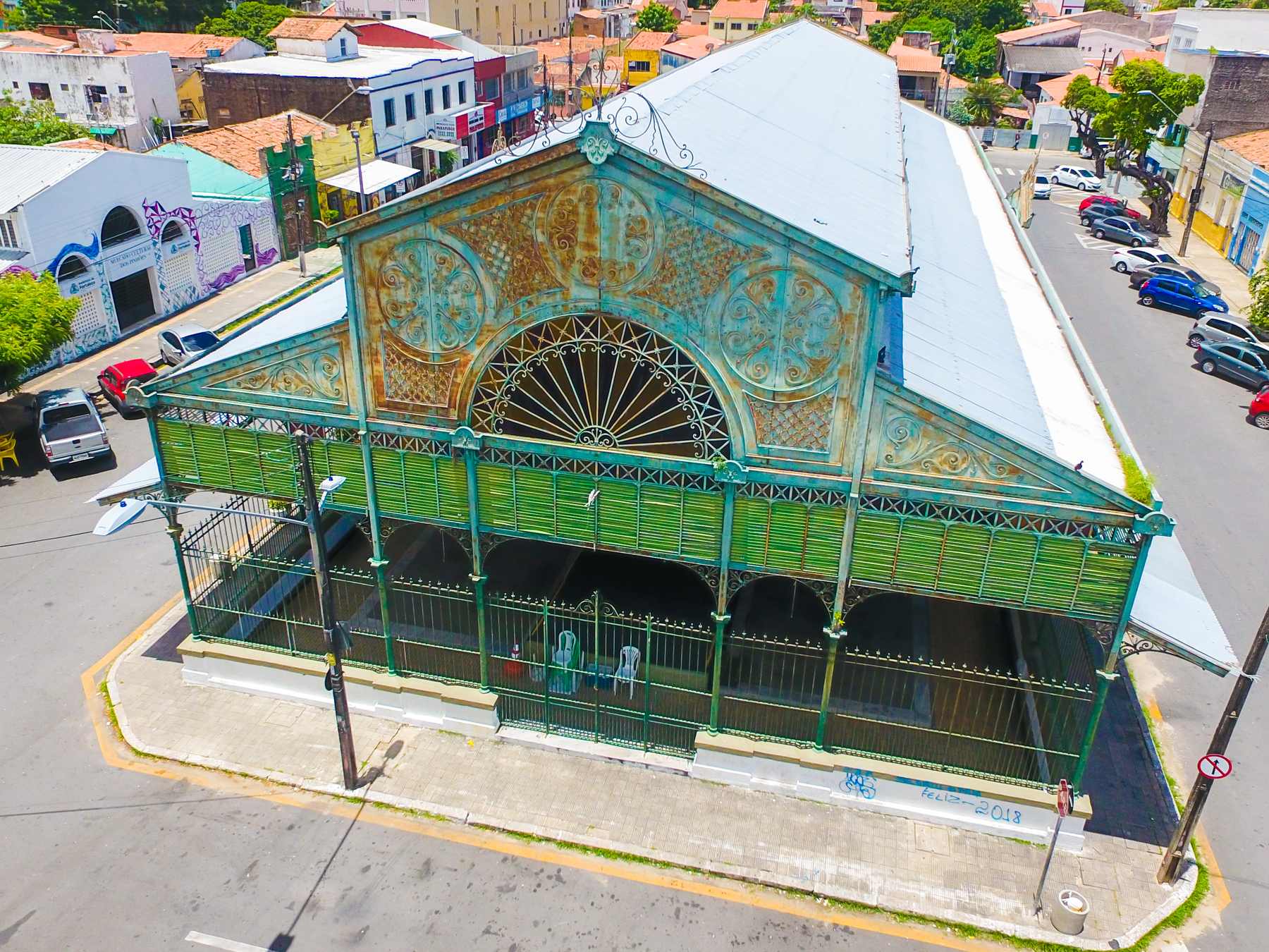 Mercado dos Pinhões visto do alto, no Centro de Fortaleza, com a estrutura de ferro verde, a fachada em leque rendado e o telhado claro entre as ruas e as árvores.