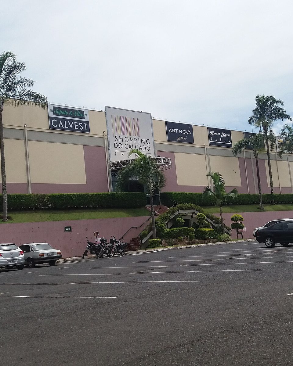 Fachada do Shopping do Calçado de Franca, com palmeiras, letreiros de lojas e o estacionamento em primeiro plano.