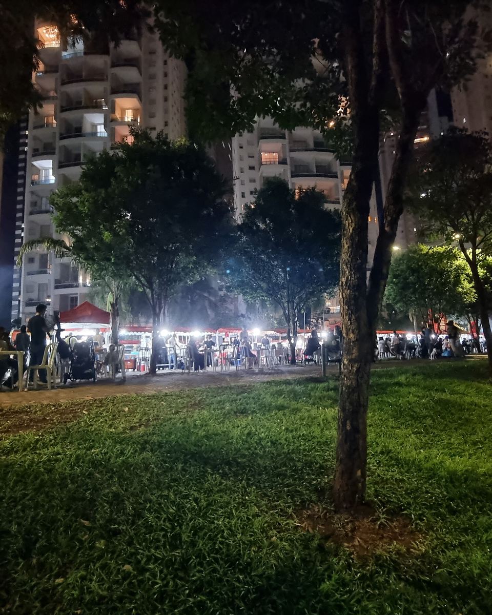 Feira noturna no Parque Flamboyant, no Jardim Goiás, com barracas iluminadas e mesas cheias de gente.