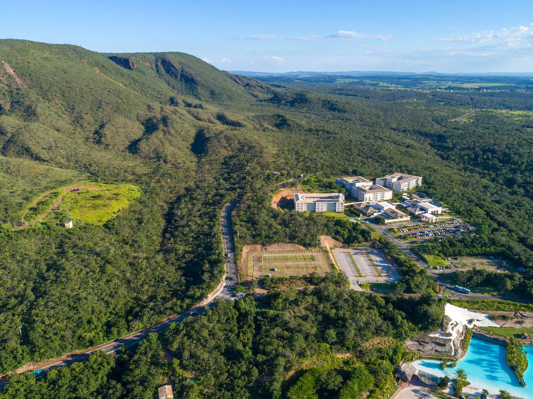 Vista aérea de Rio Quente, com a serra coberta de mata, os hotéis entre as árvores e as piscinas azuis de um parque de águas quentes.