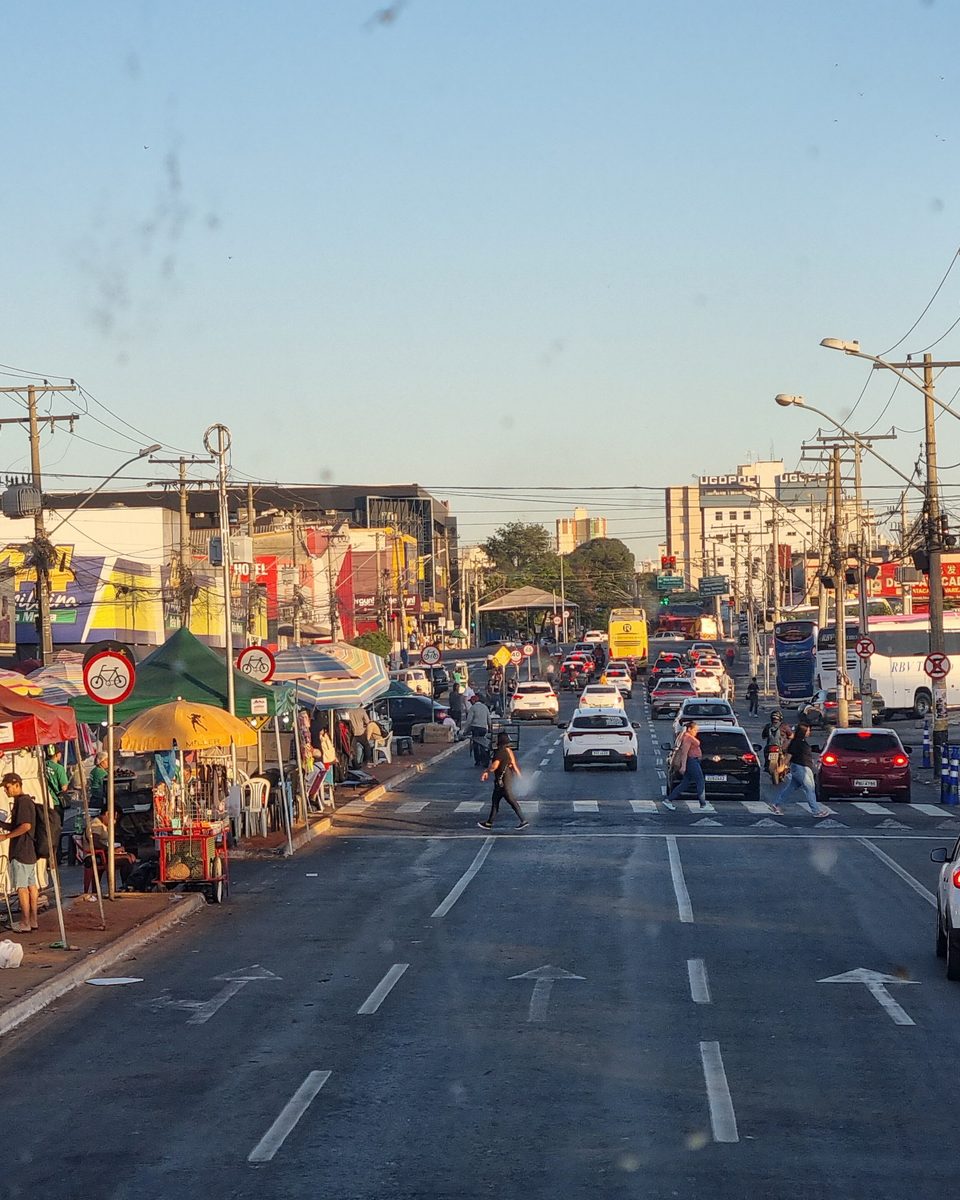 Rua 44, em Goiânia, com barracas de toldo vermelho e verde na calçada, galerias e lojas dos dois lados da avenida, carros e pessoas atravessando no fim da tarde.