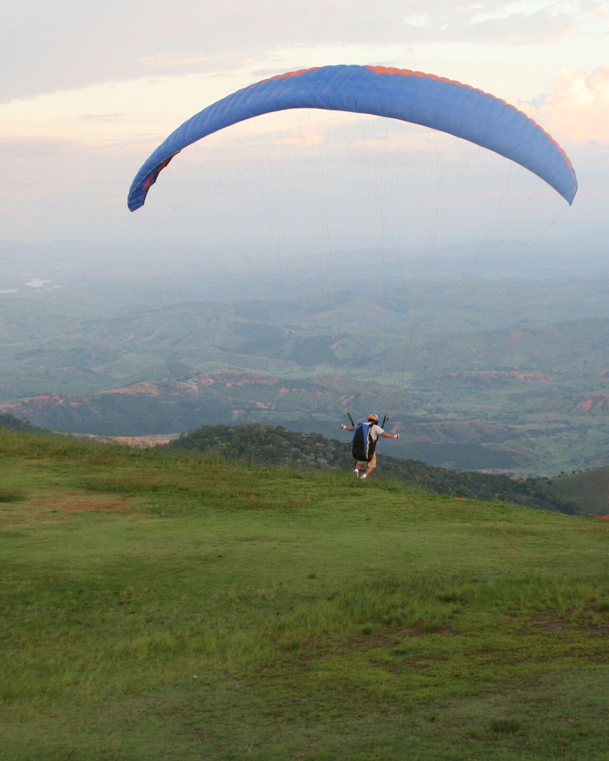 Piloto inflando um parapente azul no gramado de decolagem do Pico da Ibituruna.
