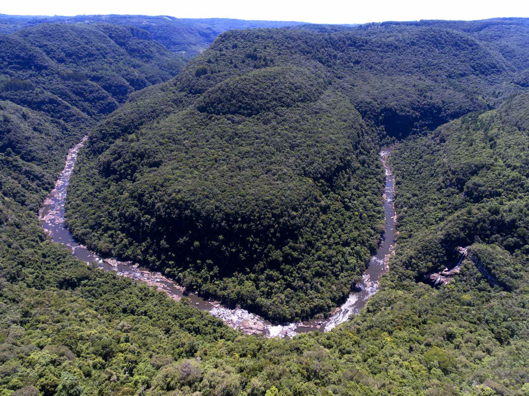 Vista aérea do Parque da Ferradura, com o rio fazendo uma curva em forma de ferradura no fundo do cânion coberto de mata.