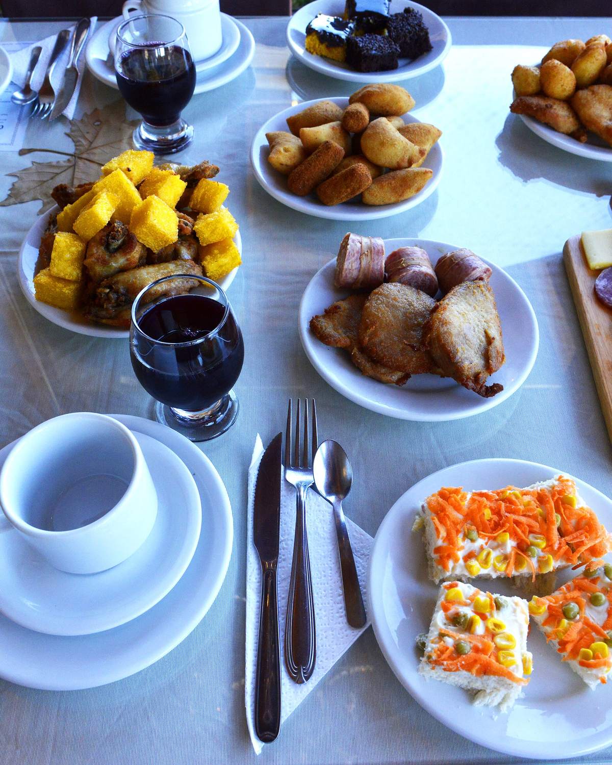 Mesa de café colonial posta com toalha branca, xícaras, taças de suco de uva, cucas, pastéis, frios, queijos e doces, em Canela.
