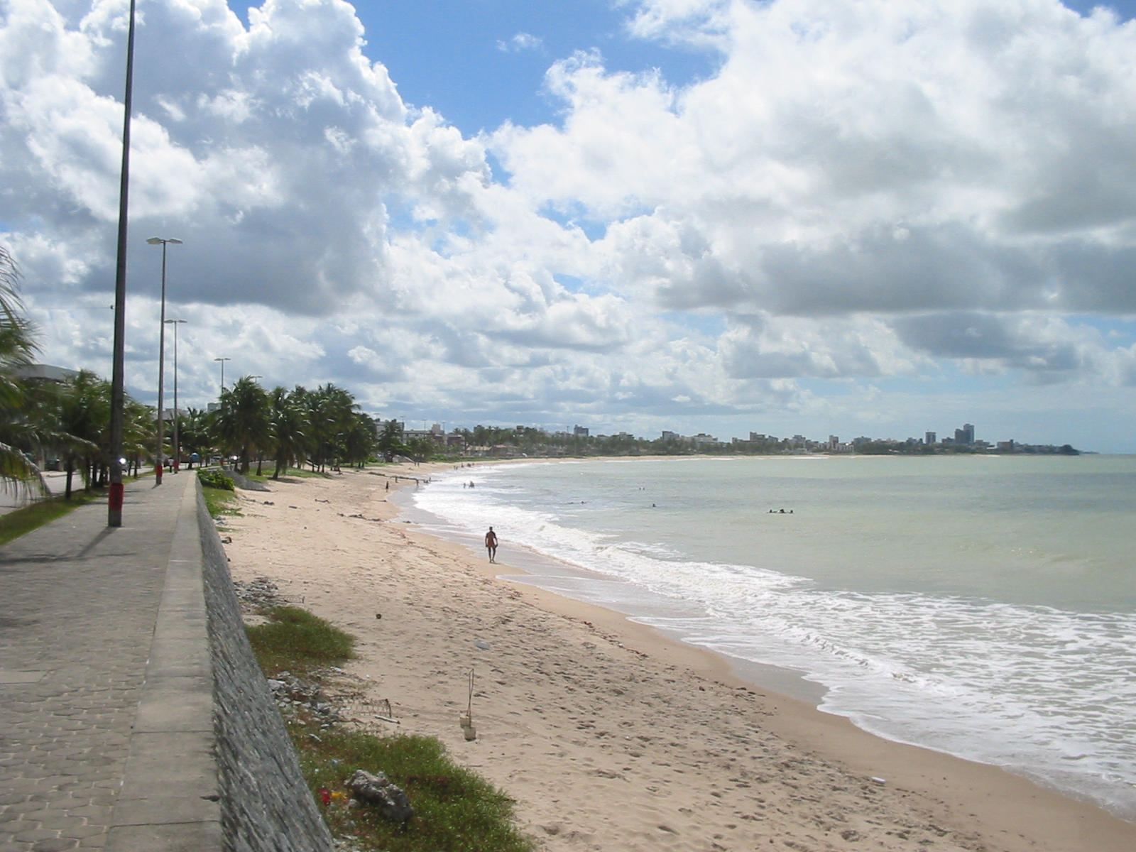 Vista da praia de Manaíra em João Pessoa, com banhistas na areia e na beira-mar e a praia do Bessa se estendendo ao fundo