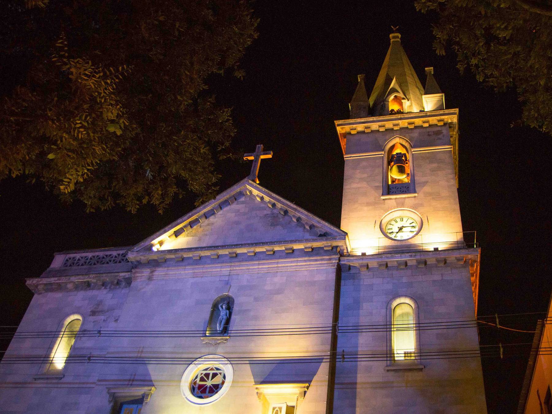 Igreja de São Sebastião iluminada à noite no Largo de São Sebastião, em Manaus, com a torre do relógio e o frontão em pedra recortados contra o céu escuro