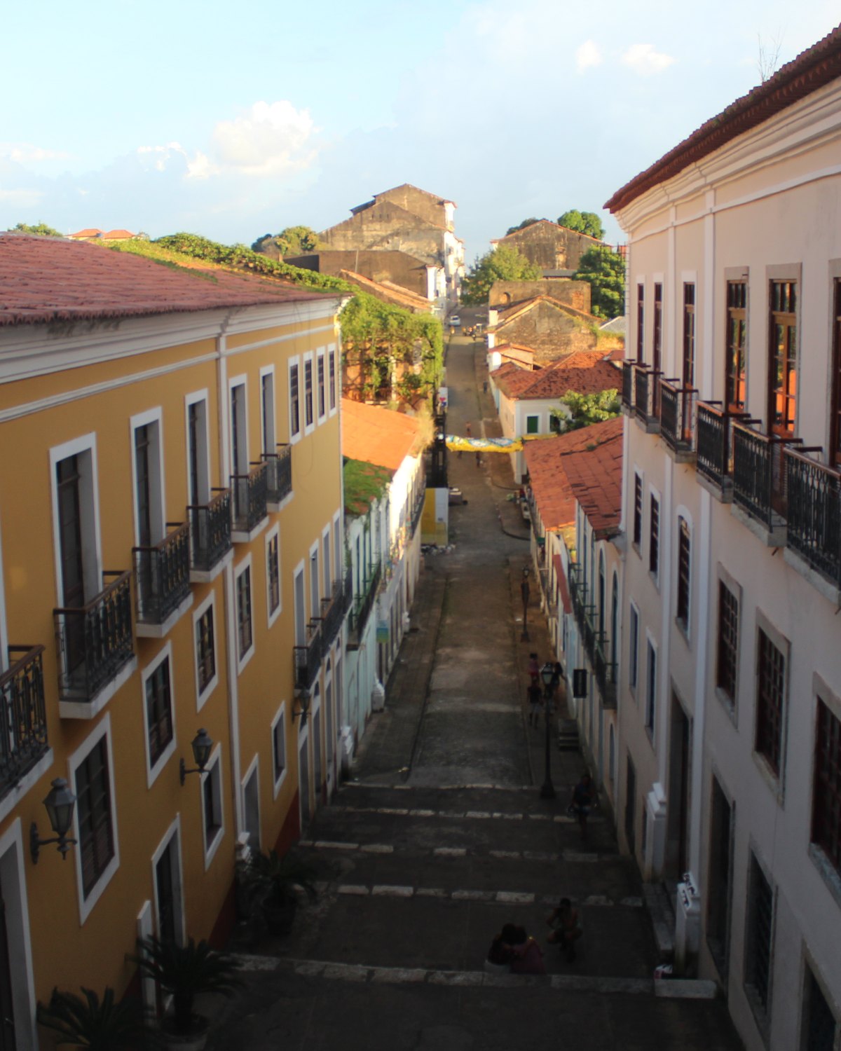 Rua em ladeira do Centro Histórico de São Luís entre casarões coloniais amarelos e brancos com sacadas de ferro e escadaria de pedra ao fundo