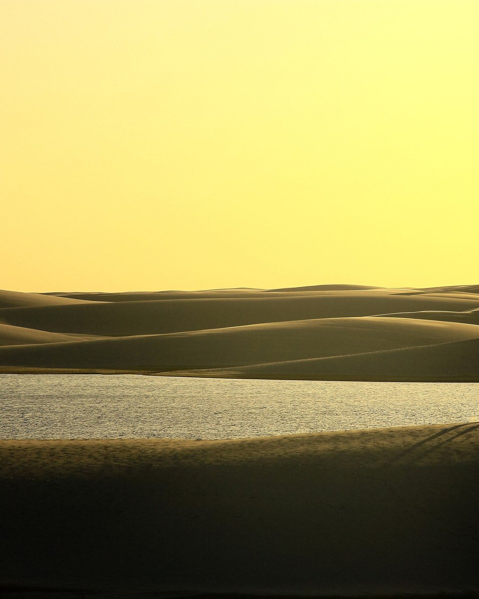 Duas pessoas caminhando sobre uma duna dos Lençóis Maranhenses no fim da tarde, com o campo de dunas se estendendo até o horizonte