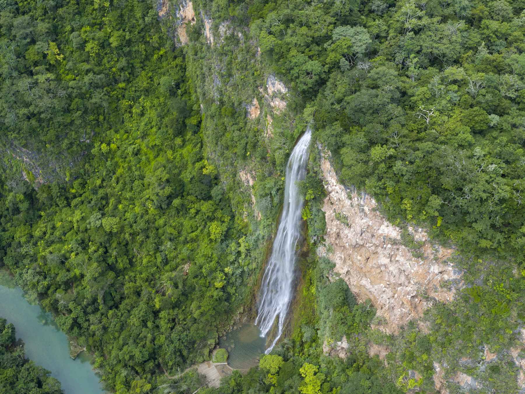 Vista aérea da cachoeira Boca da Onça caindo do paredão da serra para o cânion verde, com o rio de água esverdeada ao lado
