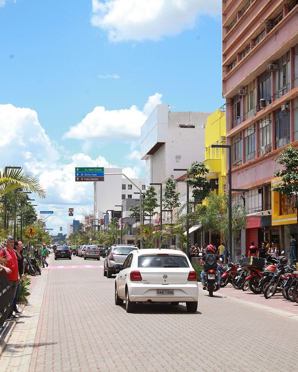 Rua 14 de Julho no centro de Campo Grande com lojas, motos estacionadas, pedestres na calçada e placa indicando a Feira Central.
