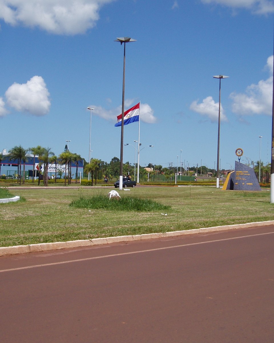 Fronteira seca entre Ponta Porã e Pedro Juan Caballero, com as bandeiras do Brasil e do Paraguai e o marco divisório no canteiro central da avenida.