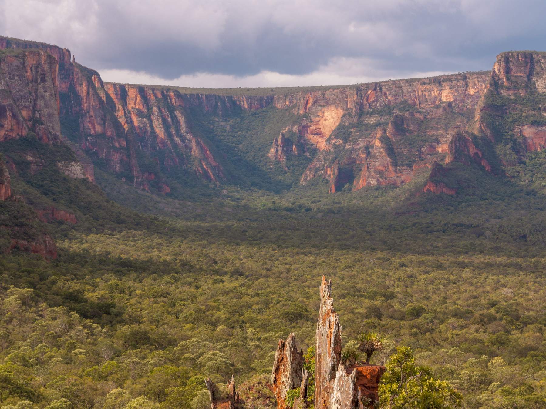 Vale do Rio Claro na Chapada dos Guimarães visto da Crista do Galo, com o anfiteatro de paredões vermelhos ao fundo, o vale de cerrado verde no meio e nuvens escuras de chuva no céu
