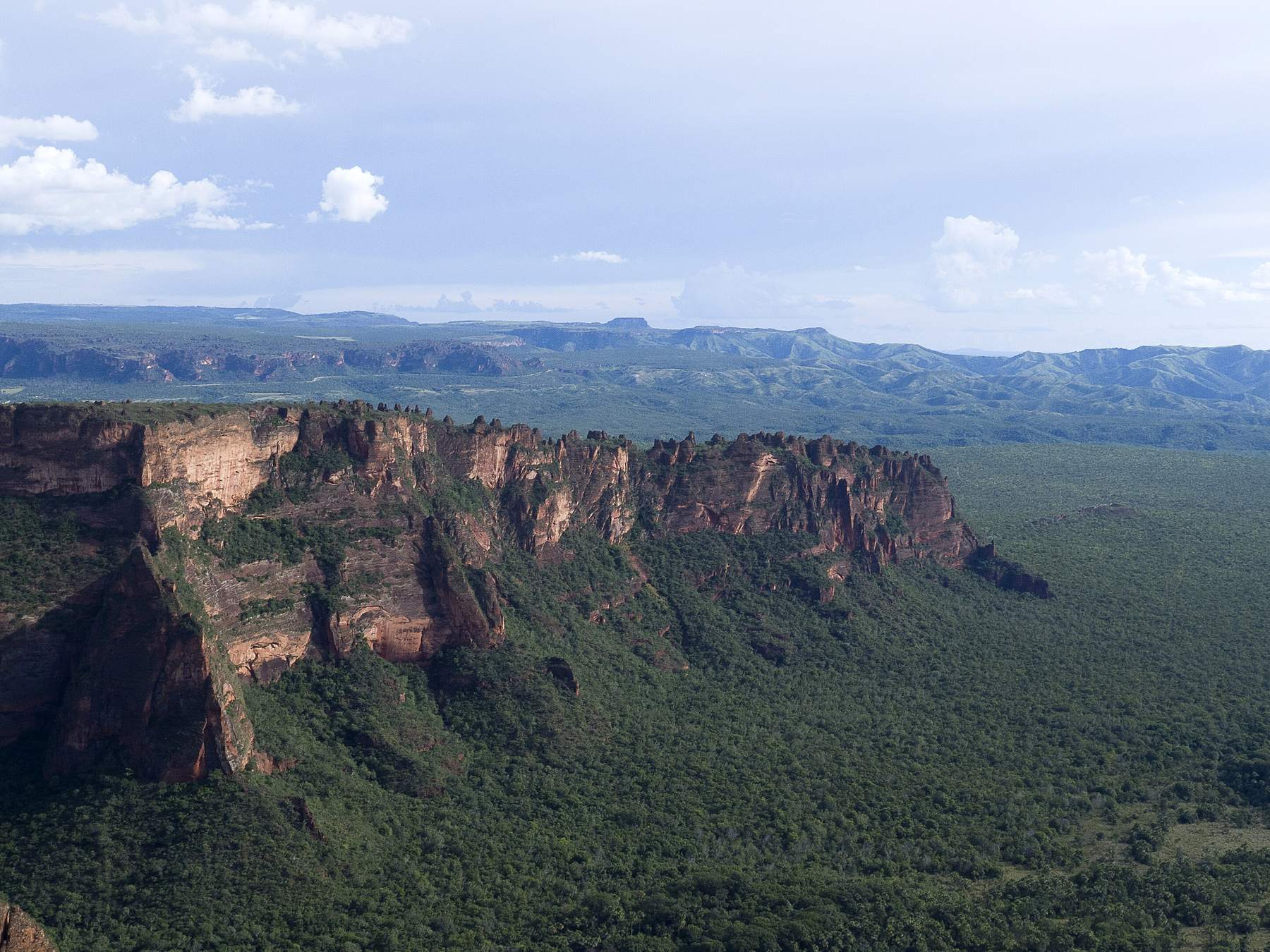 Formações rochosas da Cidade de Pedra na Chapada dos Guimarães, com a linha de paredões avermelhados recortados em torres sobre a planície coberta de mata e serras ao longe
