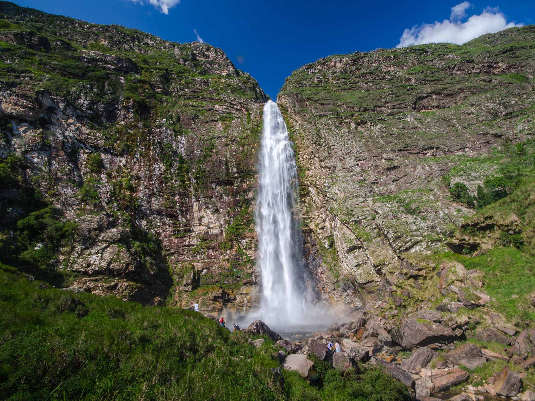 Cachoeira Casca d'Anta despencando entre dois paredões verdes, com céu azul, na Serra da Canastra.