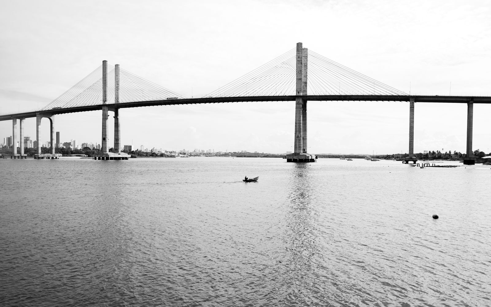 Ponte Newton Navarro em preto e branco, com os cabos estaiados sobre o rio Potengi e um barco de pescador passando por baixo