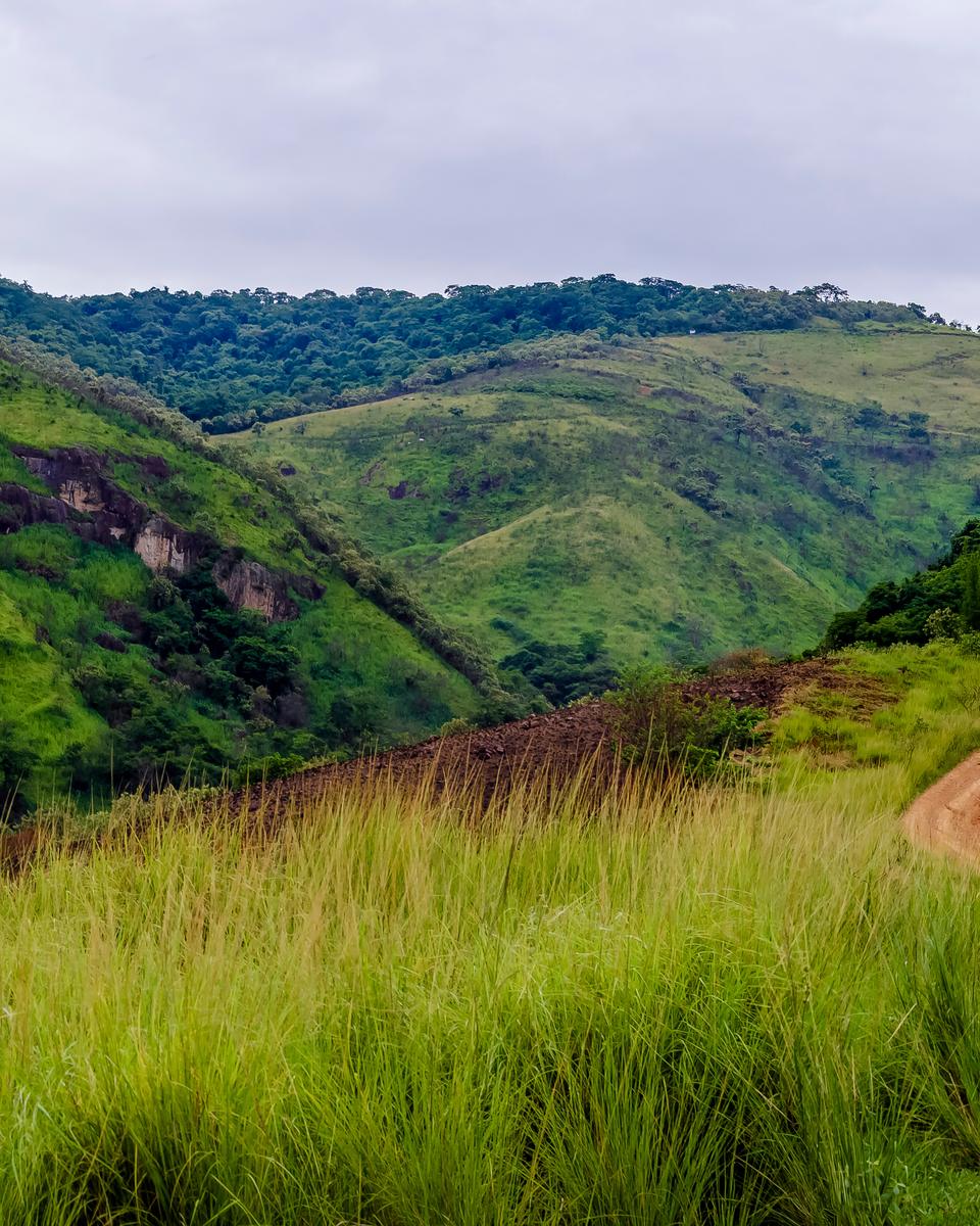 Morros verdes e estrada de terra na área rural de Nova Iguaçu, sob céu nublado.