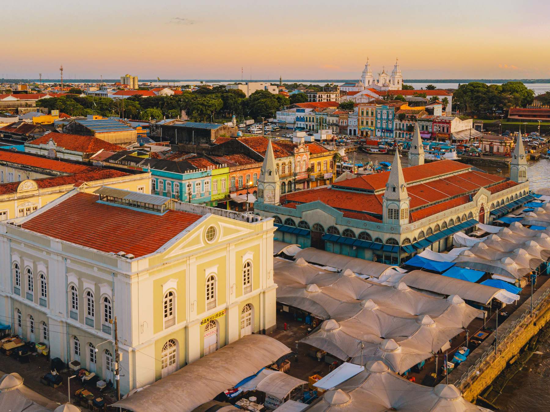 Vista aérea do Ver-o-Peso no fim da tarde, com o Mercado de Ferro, as barracas brancas da feira, os casarões coloridos da Cidade Velha e a baía do Guajará ao fundo