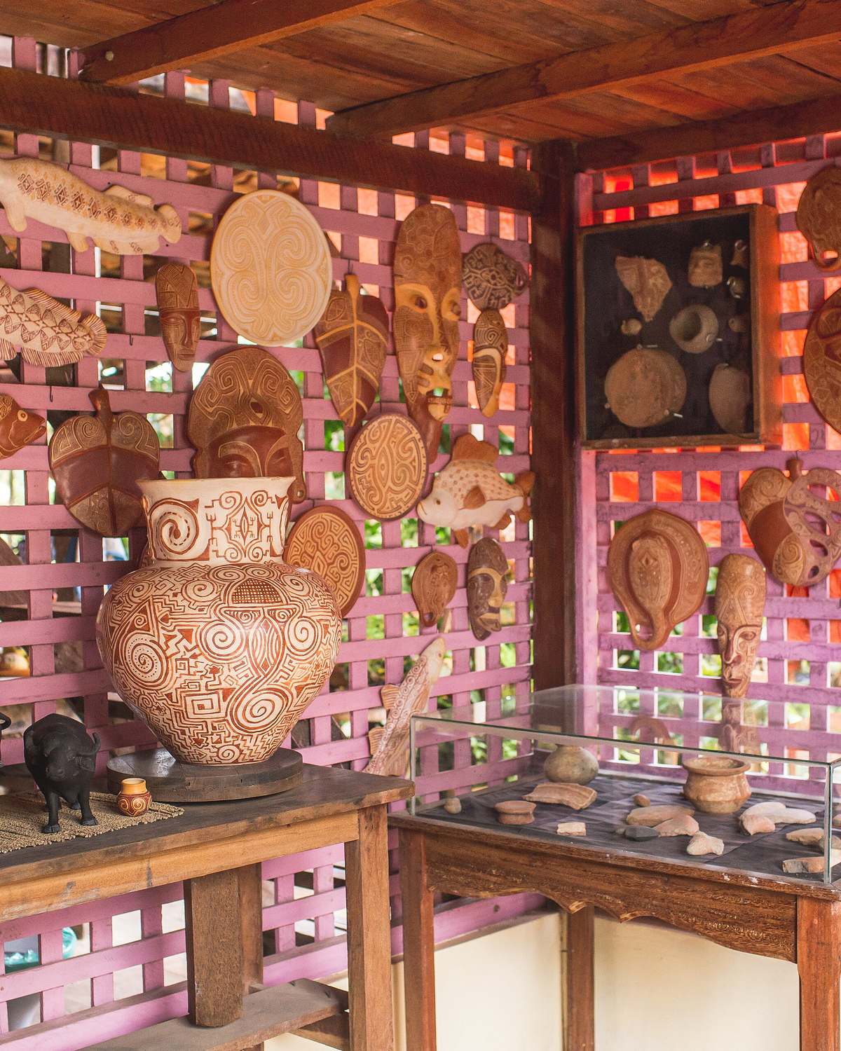 Peças de cerâmica marajoara com grafismos geométricos penduradas na parede de treliça de um ateliê em Soure, com um vaso grande e bufalinhos de barro sobre as mesas.