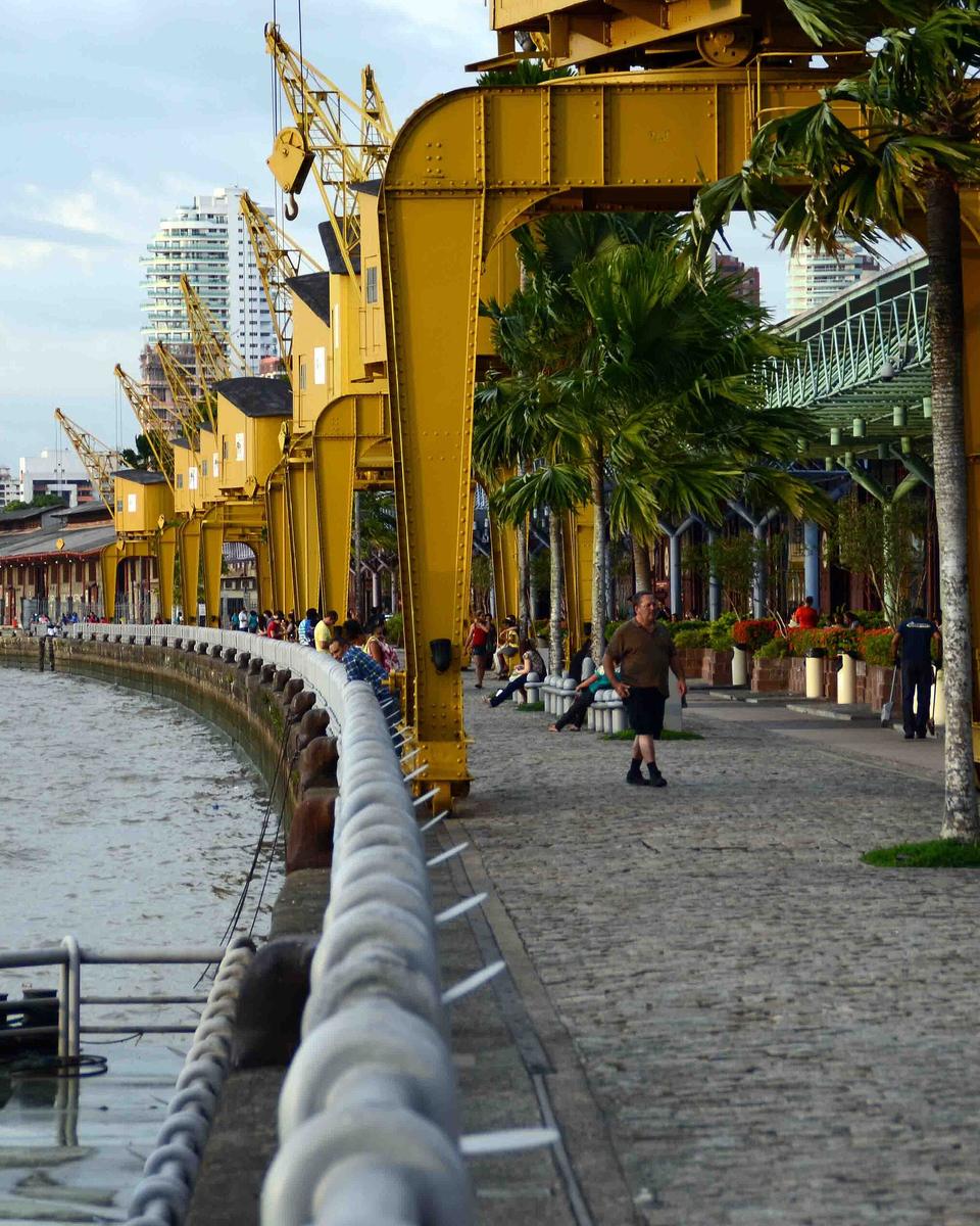 Calçadão da Estação das Docas ao entardecer, com os guindastes amarelos do antigo porto, os galpões restaurados e pessoas caminhando.