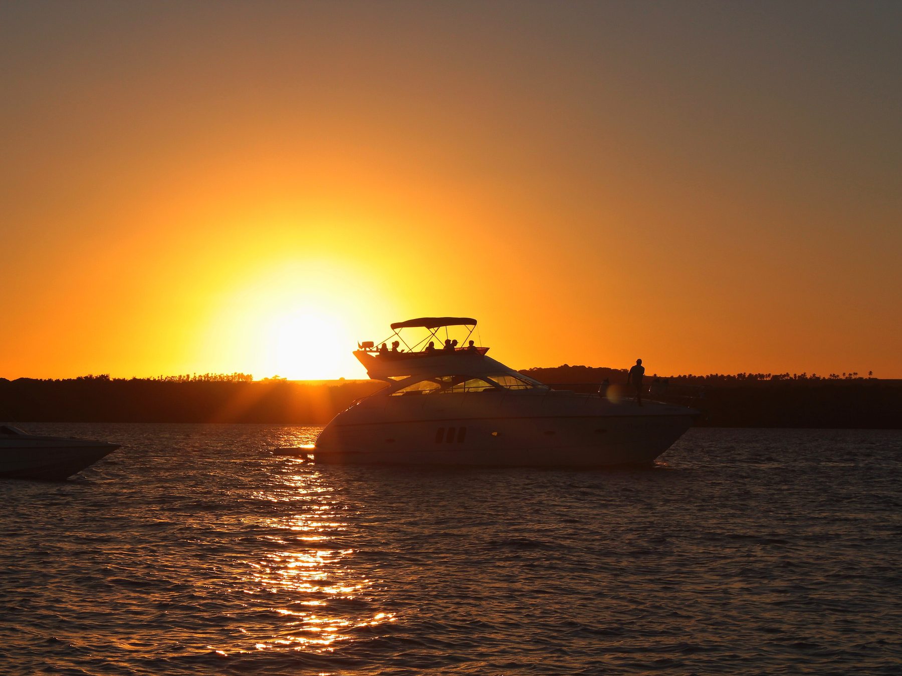 Pôr do sol na Praia do Jacaré, em Cabedelo, com o sol descendo sobre o rio Paraíba e a silhueta de um barco de passeio na água