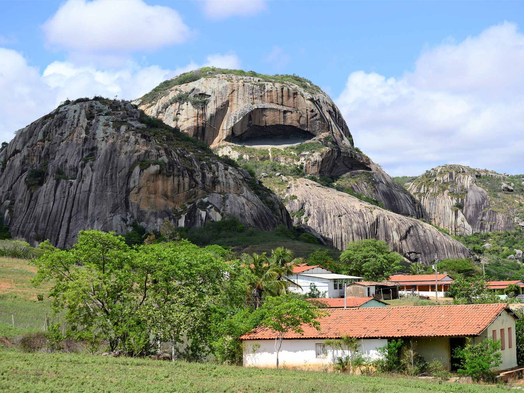 Paredões de granito da Pedra da Boca, em Araruna, com a grande abertura em forma de boca na rocha e casas de telhado vermelho ao pé do morro