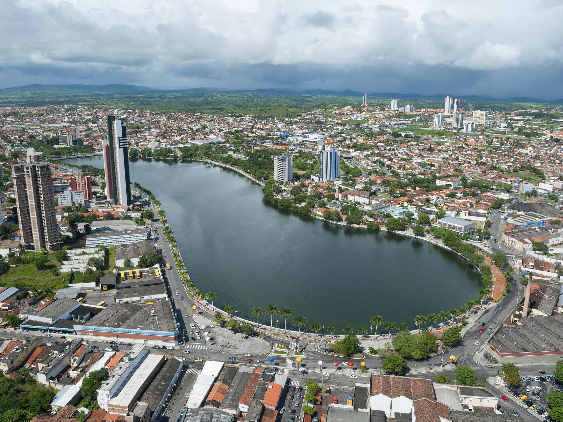 Vista aérea do Açude Velho, em Campina Grande, com o espelho d'água cercado por coqueiros e pelas avenidas e prédios da cidade